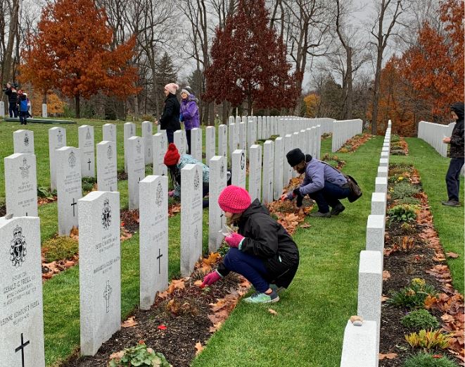 School aged child placing a single poppy on the grave of a Canadian Armed Forces Member