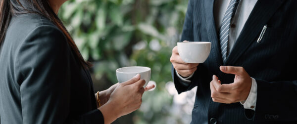 Coffee break. Group business people, standing in modern office, holding a cups, smiling standing at the window